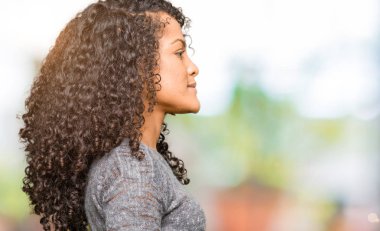 Kıvırcık saçlı genç güzel kadın yan bakıyor gri kazak giyiyor, kendine güvenen gülümseme ile doğal yüzü ile profil poz rahatlayın.