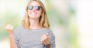 Izole arka plan üzerinde güneş gözlüğü takan güzel genç kadın çok mutlu ve heyecanlı kolları kaldırdı ile kazanan jest yapıyor, gülümseyerek ve başarı için çığlık. Kutlama konsepti.