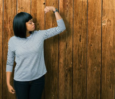 Giyen güzel genç Afro-Amerikan kadın kazak kol kasları gururlu gülümseyen gösterilen izole arka plan üzerinde çizgili. Fitness kavramı.