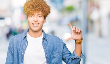 Genç yakışıklı adam afro saç giyen denim ceket gülümseyen ve emin işaret ile el yapıyor boyutu işareti yaparken parmaklar ve kamera bakıyor. Ölçü kavramı.
