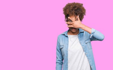 Mahcup ifadeyle parmaklarımın arasından yüz ve gözler el ile kapsayan şok bakmak izole arka plan üzerinde gözlük güzel genç Afro-Amerikan kadın arıyor.