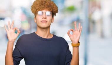 Afro gözlük sakin ol genç yakışıklı adamla ve gülümseyen gözlerle parmak ile meditasyon jest yapıyor kapalı. Yoga kavramı.