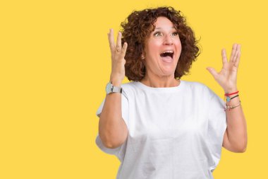 Üzerinde beyaz t-shirt giyen güzel orta ager üst düzey kadın deli kutluyor arka plan izole ve başarı için kaldırdı kollarını açarak hayrete ve heyecanlı çığlık gözleri açık. Kazanan kavramı