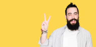 Uzun saç, sakal ve mutlu yüz zafer işareti yaparken kameraya göz kırpıyor ile gülümseyen küpe olan genç adam. İki numaralı.