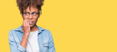 Stresli ve gergin elle çivi ısırma ağzına bakarak izole arka plan üzerinde gözlük güzel genç Afro-Amerikan kadın. Anksiyete sorunu.