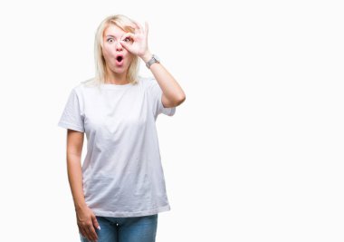 Sürpriz yüz, göz parmaklarının arasından seyir ile ok jest yapıyor izole arka plan üzerinde beyaz t-shirt giyen genç güzel sarışın kadın şok. İmansız ifade.