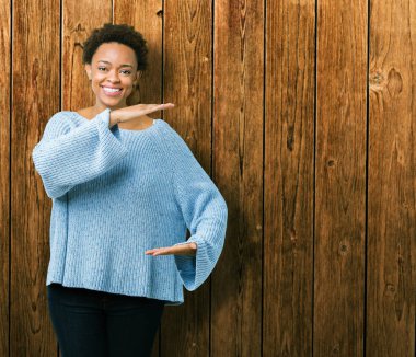 İle büyük ve büyük boy işaret, ölçü birimi sembol gösteren el eller izole arka plan üzerinde bir kazak giyen genç güzel Afrikalı-Amerikalı kadın. Kameraya bakarak gülümsüyordu. Ölçüm kavramı.