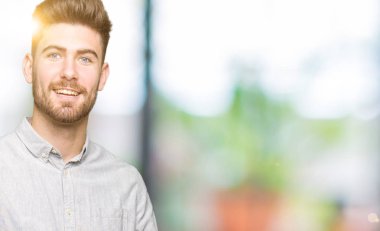 Genç ve yakışıklı bir adam gündelik gömleğini giyerken kameraya hayret ediyor ve gülümsüyor..