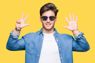 Yakışıklı delikanlı üzerinde güneş gözlüğü takıyor gösterilen arka plan izole ve parmakları ile işaret kendinden emin ve mutlu gülümseyerek süre 8 numaralı.
