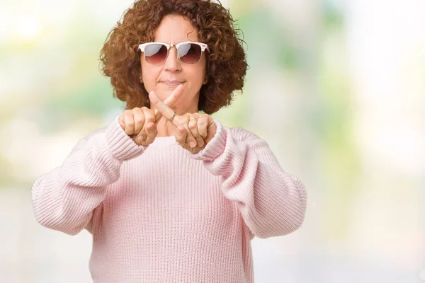 美丽的中年老年妇女穿着粉红色毛衣和太阳镜在孤立的背景拒绝表达交叉手指做负号 — 图库照片