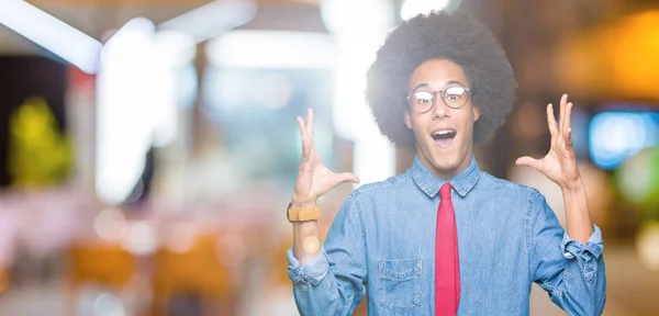 若いアフリカ系アメリカ人ビジネスの男性眼鏡と赤いアフロの髪と祝う狂気を結ぶし 叫んで興奮発生と開いた目の腕の成功のため驚きます 勝者の概念 — ストック写真