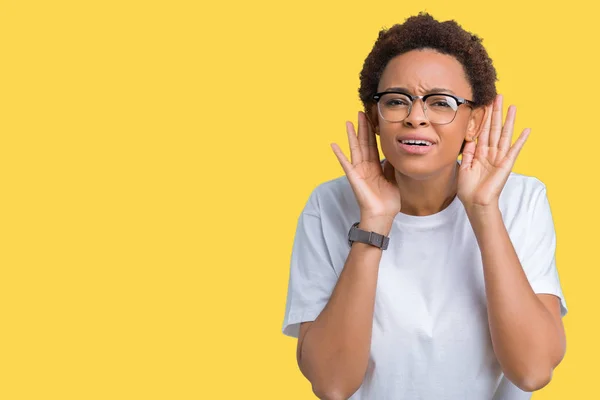 Beautiful young african american woman wearing glasses over isolated background Trying to hear both hands on ear gesture, curious for gossip. Hearing problem, deaf