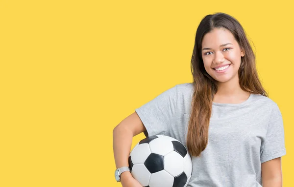 年轻美丽的黑发女子拿着足球在孤立的背景与幸福的脸站在和一个自信的微笑显示牙齿 — 图库照片
