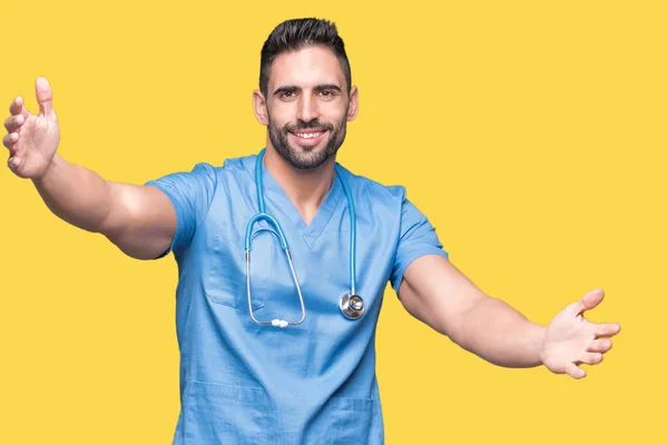 英俊的年轻医生外科医生男子在孤立的背景看着相机微笑着张开双臂拥抱 拥抱幸福的欢快表达 — 图库照片