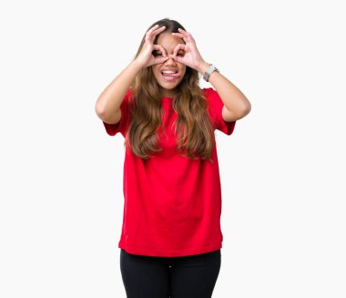 Dilini, parmaklarının arasından baktığını yapışmasını dürbün gibi ok jest yapıyor izole arka plan üzerinde kırmızı t-shirt giyen genç güzel esmer kadın. Deli ifade.