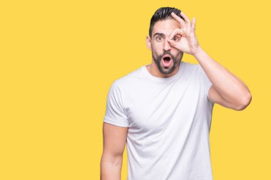 Sürpriz yüz, göz parmaklarının arasından seyir ile ok jest yapıyor izole arka plan üzerinde rahat beyaz t-shirt giyen genç adam şok. İmansız ifade.