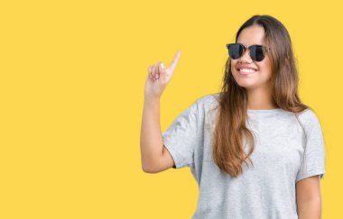 Genç güzel esmer kadın izole arka plan üzerinde güneş gözlüğü giyen başarılı bir fikir parmak yukarı işaret. Çıkıldı ve mutlu. Bir numara.