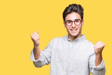 Yakışıklı delikanlı izole arka plan üzerinde kutluyor gözlük takan şaşırttı ve başarı için kaldırdı kollarını açarak hayret ve gözleri açık. Kazanan kavramı.