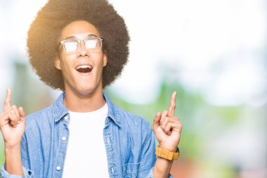 Afro saçlı gözlüklü genç Afro-Amerikan adam hayret ve yukarıya bakıyor ve parmakları ile işaret ve silah kaldırdı şaşırttı.
