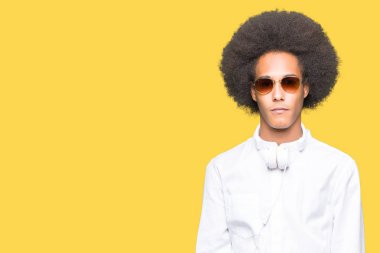 Afro saçlı Genç Afrikalı Amerikan adam yüzünde ciddi bir ifade ile güneş gözlüğü ve kulaklıklar giyiyor. Basit ve doğal kamera bakıyor.