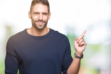 Yüz üzerinde büyük bir gülümseme ile izole arka plan üzerinde kazak giyen genç yakışıklı adam, kamera bakarak yan el ve parmak ile işaret.