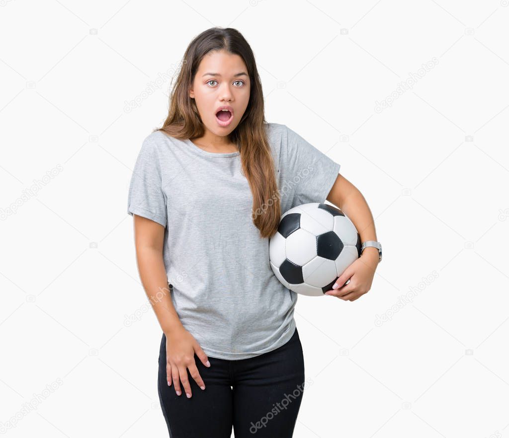 Young beautiful brunette woman holding soccer football ball over isolated background scared in shock with a surprise face, afraid and excited with fear expression