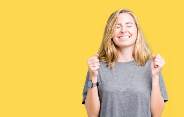 Güzel genç kadın giyiyor büyük boy rahat t-shirt izole arka plan üzerine silah ile başarı için heyecanlı zafer kutluyor gülümseyen kaldırdı. Kazanan kavramı.