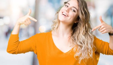 Yüzünde gülümseme ile kendinden emin görünüyorsun, kendini gururlu ve mutlu parmakları ile işaret izole arka plan üzerinde sarışın güzel genç kadın.