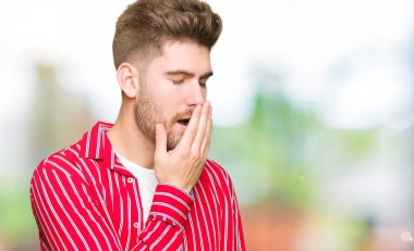 Kırmızı gömlek giymiş genç yakışıklı adam el ağzıyla kapsayan yorgun esneme sıkılmış. Restless ve uyku hali.