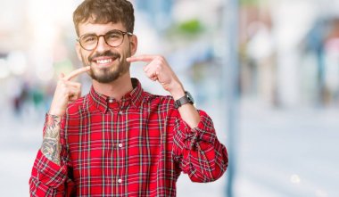 Kendinden emin gösterilen ve işaret parmakları diş ve ağız ile gülümseyen izole arka plan üzerinde gözlük takan yakışıklı delikanlı. Sağlık kavramı.
