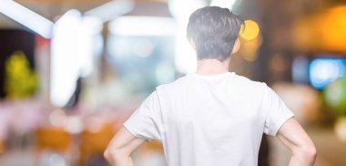 İzole arka plan ayakta geriye doğru uzakta silah ile vücut üzerinde seyir üzerinde rahat beyaz t-shirt giyen genç yakışıklı adam