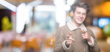 Üzerinde kış ceket giyen genç yakışıklı adam arka plan fotoğraf makinesi ile mutlu ve komik yüz için parmakları işaret izole. İyi enerji ve vibes.