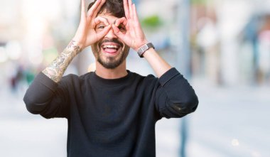 Yakışıklı delikanlı, dilini parmaklarının arasından baktığını yapışmasını dürbün gibi ok jest yapıyor izole arka plan üzerinde. Deli ifade.