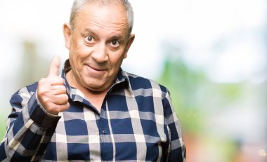 Rahat gömlek giyen yakışıklı kıdemli adam el ile jest kadar mutlu başparmak yapıyor. Başarı göstererek kameraya bakarak ifadeyi onaylama.