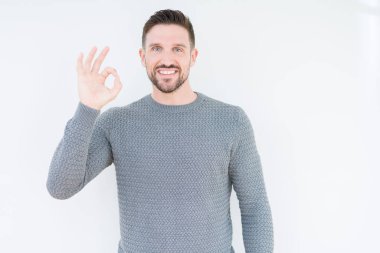 İzole arka plan üzerinde rahat kazak giyen genç yakışıklı adam el ve parmaklar ile ok işareti yapıyor pozitif gülümseyen. Başarılı ifade.