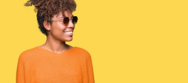 Güzel genç Afro-Amerikan kadın uzak tarafına yüzünde, doğal ifade gülümseme ile seyir izole arka plan üzerinde güneş gözlüğü takıyor. Kendine güvenen gülüyor.