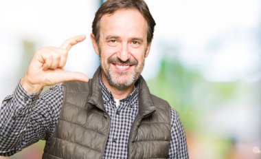 Orta Çağ yakışıklı adam kış yelek giyen gülümseyen ve emin el ile boyut işareti yaparken parmaklar ile görünümlü ve kamera bakıyor. Ölçü kavramı.