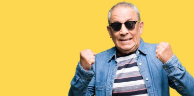 Denim ceket ve kutlama güneş gözlüğü takan yakışıklı komuta sizde şaşırttı ve başarı için kaldırdı kollarını açarak hayret ve gözleri açık. Kazanan kavramı.