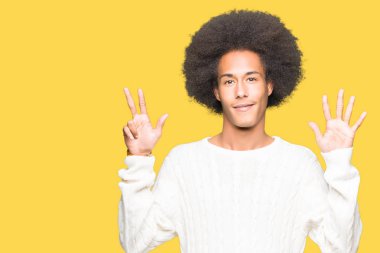 Afro saç içeren genç Afrikalı Amerikalı adam kış kazak gösteren ve parmak sayısı sekiz ile işaret kadar kendine güvenen ve mutlu gülümseyen.