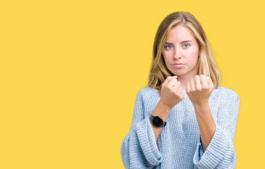 Güzel genç kadın giyiyor mavi kazak izole arka plan üzerinde yumruk savunma hareketi, kızgın ve üzgün yüz, sorunu korkuyor ile savaşmaya hazır