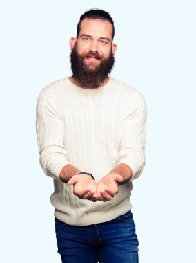 Kışlık kazak giyen genç hipster adam el avuç içi birlikte alma veya jest vererek gülümsüyor. Tutma ve koruma