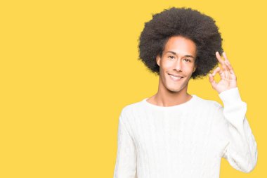 Afro saç giyen kış kazak el ve parmaklar ok işaretiyle yapıyor olumlu gülümseyen genç Afro-Amerikan adam. Başarılı ifade.