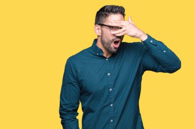 Yüz ve gözler el ile kapsayan şok izole arka plan bakmak üzerinde gözlük takan genç yakışıklı iş adamı mahcup ifadeyle parmaklarımın arasından arıyorsunuz.