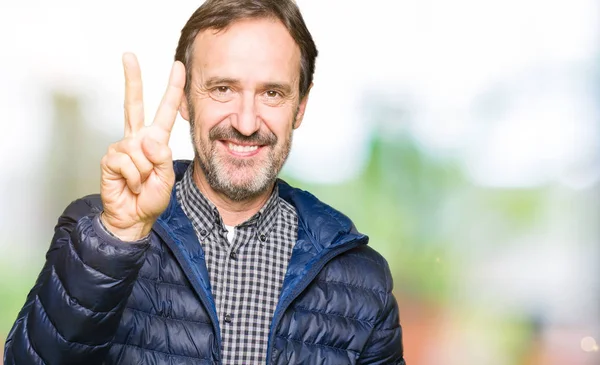 Orta Çağ yakışıklı adam kış ceket gösteren giyen ve parmak sayısı iki ile işaret kadar güven ve mutlu gülümseyen.