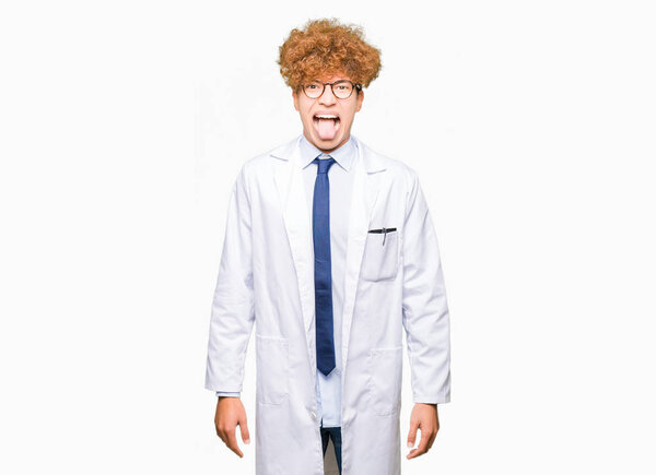 Young handsome scientist man wearing glasses sticking tongue out happy with funny expression. Emotion concept.