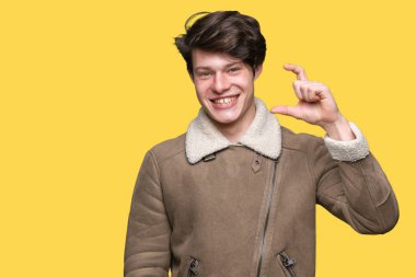 Genç yakışıklı adam üzerinde kış ceket giyiyor izole arka plan gülümseyen ve emin işaret ile el yapıyor boyutu işareti ile parmak görünümlü ve kamera. Ölçü kavramı.