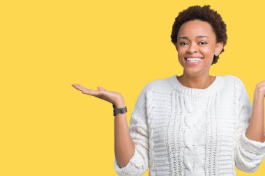 Gülen iki elle gösterilen açık avuç içi, sunma ve karşılaştırma ve denge reklam arka plan üzerinde kazak giyen güzel genç Afro-Amerikan kadın izole