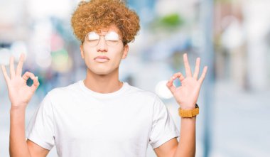 Afro saç ile genç yakışıklı adam gözlük giymek rahatlayın ve gözleri ile gülümseyen meditasyon jest parmaklar ile kapalı. Yoga konsepti.