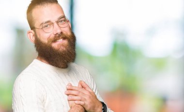 Gözlük ve ile gülümseyen kış kazak giyen genç hipster adam kapalı gözler ve yüzünde minnettar jest ile göğüs üzerinde eller. Sağlık kavramı.