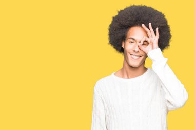 Afro saç giyen kış kazak ile genç Afrikalı Amerikalı adam el gülümseyen ok jest yapıyor, göz mutlu yüz ile parmaklar görünümlü.